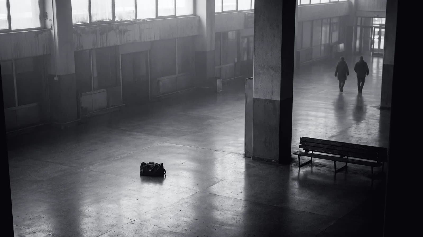 Illustrative frame: a transport concourse floor with a single bag left alone on it, and computer vision marking it as unattended with the time it has been stationary. Shown in black and white, with the annotated regions revealed in colour.